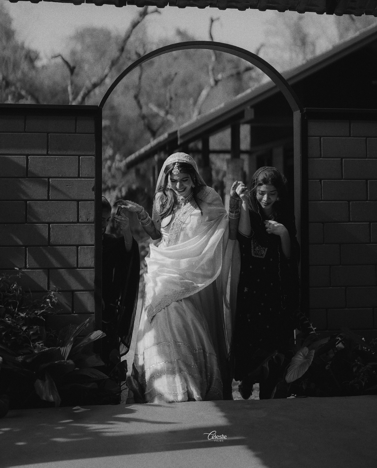 Bride walking with a companion beneath a garden arch